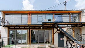 Un edificio moderno de dos pisos con fachada de madera, amplios ventanales de vidrio y una escalera que conduce al nivel superior.