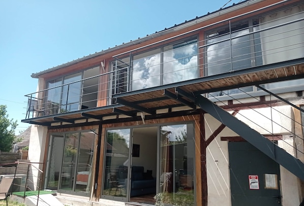 Edifici de dues plantes amb un balcó, grans portes corredisses de vidre i una escala.
