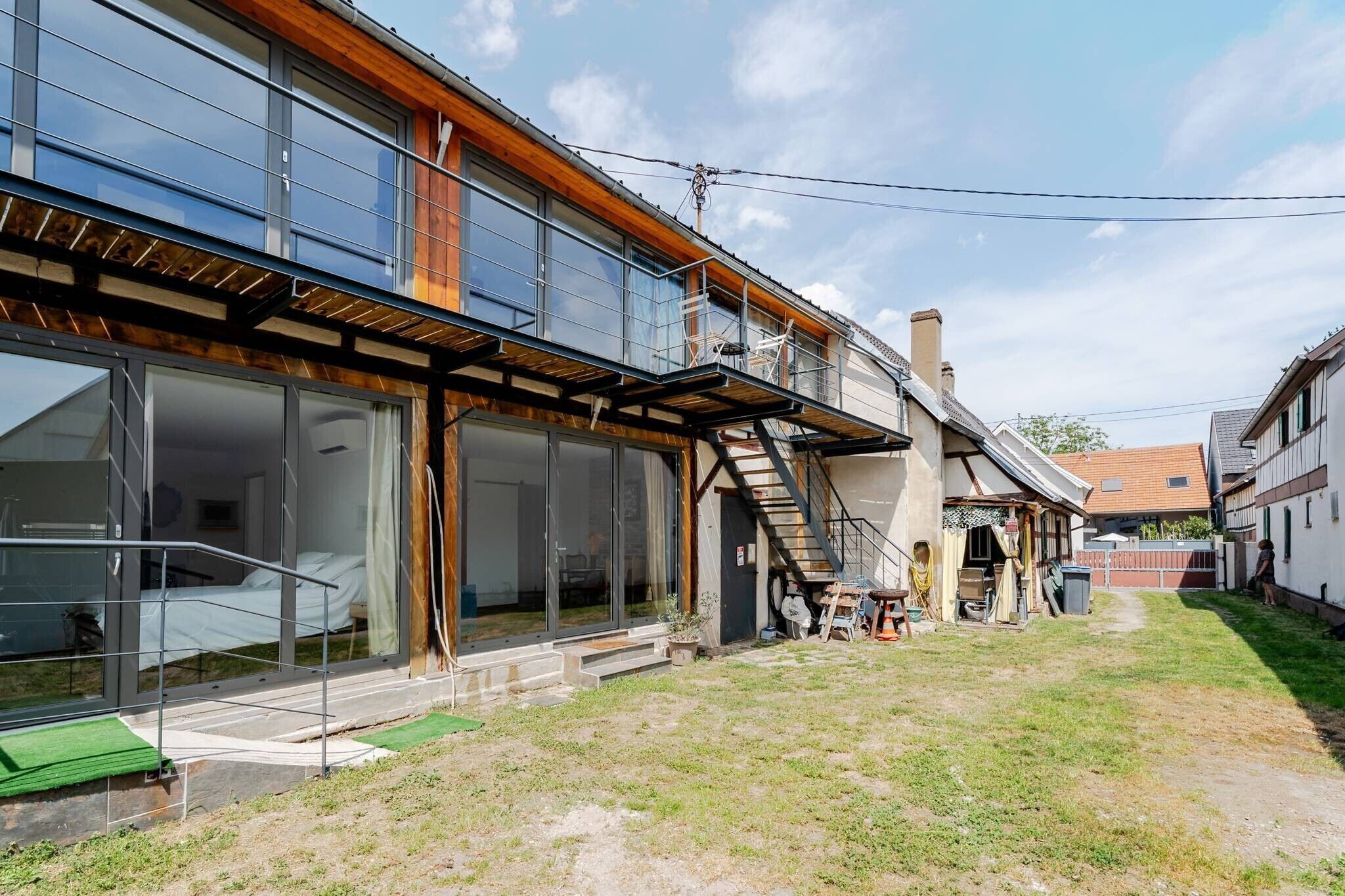 A modern house with a large glass window, a wooden deck, and a staircase leading to the upper floor.
