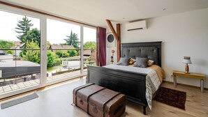 Un dormitorio con un gran ventanal corredero, una cama con cabecera estampada, un banco y una maleta.
