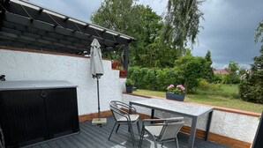 Una veranda esterna con tavolo e sedie, una pergola e piante in vaso.