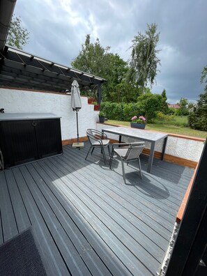 Een terras buiten met een tafel, stoelen, een pergola en potplanten.