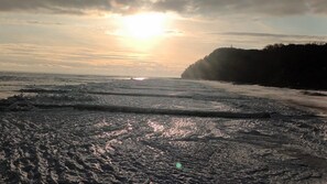 Een strand met golven, een zonsondergang en een beboste klif.