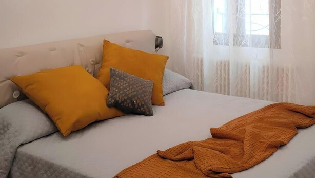 A bed with a white headboard, two mustard-colored pillows, a gray patterned pillow, and a mustard-colored blanket. - Room 'Bovoletto Camera Doppia - Aqua Alta' with Wi-Fi and Air Conditioning (Chioggia)