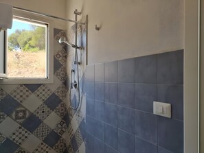 Ein Badezimmer mit Dusche, gemusterten Fliesen, einem Fenster und einem Lichtschalter.