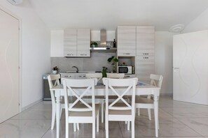 A modern kitchen with white cabinetry, a dining table with four chairs, and a built-in microwave.