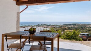 Ein Holztisch mit Stühlen und einer Fruchtschale, mit Blick auf eine malerische Landschaft, Meer und Hügel.