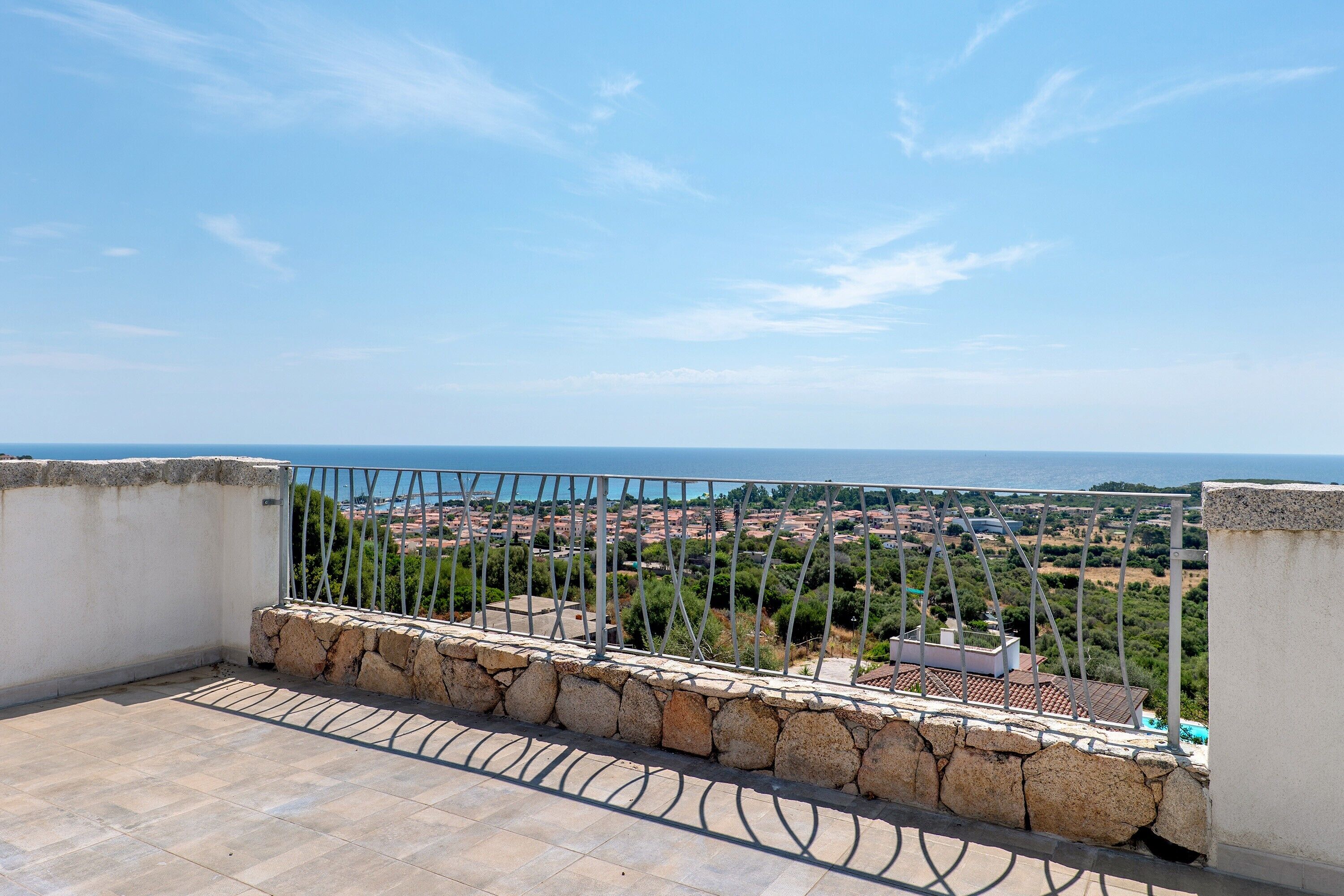 A balcony with stone walls and metal railing overlooking a coastal town.