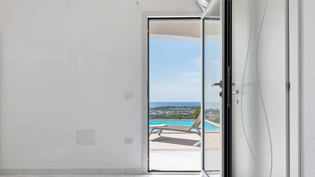 Ein Schlafzimmer mit Bett, einer Schiebetür zu einem Balkon mit Pool und Liegestühlen.
