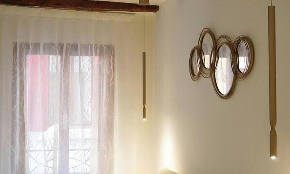 Une pièce dotée d’une grande fenêtre, d’un luminaire suspendu et de trois miroirs fixés au mur.