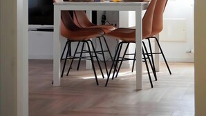 Een moderne eethoek met een witte tafel, bruine stoelen, een televisie en een houten trap.