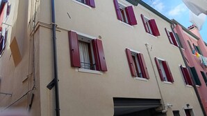 Een meerlaags gebouw met rode luiken bij de ramen, een zichtbaar balkon en een plat dak.