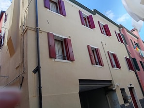 Ein mehrgeschossiges Gebäude mit roten Fensterläden, einem sichtbaren Balkon und einem flachen Dach.
