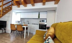 Une cuisine moderne avec des meubles blancs, un coin repas comprenant une table et des chaises, et un salon avec un canapé.