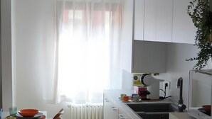 Een moderne keuken met witte kasten, een inbouwoven en een raam met dunne gordijnen.