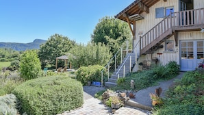 A rustic building with a wooden balcony, a stone staircase, and a garden with various plants and a gazebo.