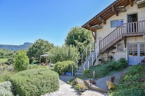 A rustic building with a wooden balcony, a stone staircase, and a garden with various plants and a gazebo.