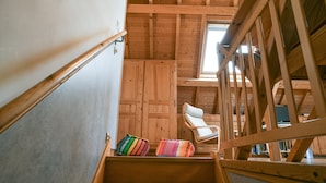 A wooden staircase with a view of a room with a white chair and colorful cushions.