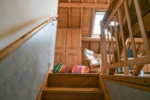 A wooden staircase with a view of a room with a white chair and colorful cushions.