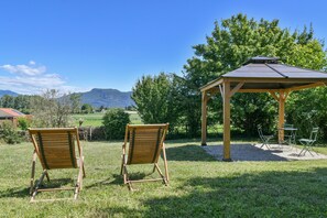 Due sedie di legno in un prato con un gazebo e vista sulle montagne.