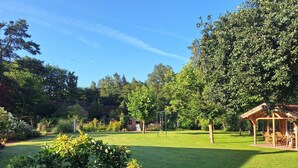 Hyvin hoidettu puutarha, jossa on puinen pergola, lintulautaa ja monenlaisia kasveja.