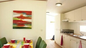 Ein Essbereich mit Tisch für zwei Personen, grünen Stühlen und einem farbenfrohen, abstrakten Gemälde an der Wand.