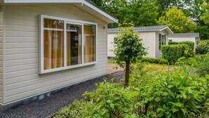 Ein Bungalow mit großem Fenster, umgeben von viel Grün und Bäumen.