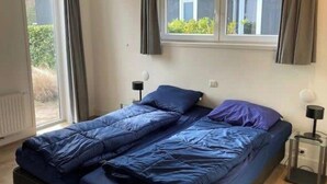 A room with a bed, two bedside tables, a window with curtains, and a radiator. - Holiday Home in Brunssum With Terrace (Brunssum)