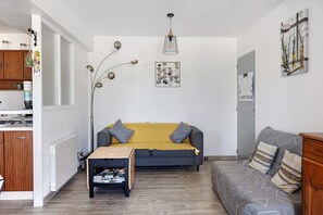 Uma sala de estar com sofá, mesa de centro e um espaço de jantar, com cozinha visível ao fundo.