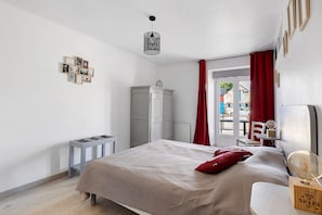 Une chambre à coucher avec un lit, une petite table, une armoire et une fenêtre avec des rideaux rouges.