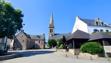 Une place de ville bordée de bâtiments historiques, avec un clocher d’église et un panneau indicateur indiquant les directions.