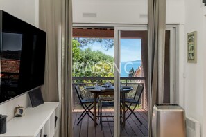 A balcony with a table and chairs, a television, and a trash can. - Apartment 'Sea View  A Short Walk To' with Sea View, Shared Terrace and Air Conditioning (Rayol-Canadel-sur-Mer)