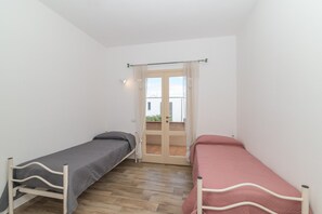 A small room with two single beds, a wooden floor, a window with curtains, and a door leading outside. - Apartment 'Casa Del Porto' with Private Terrace and Air Conditioning in Central Palau (Palau)