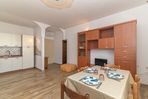 Un coin repas avec une table dressée pour quatre personnes, des meubles en bois et une cuisine en arrière-plan.