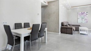 Una sala de estar moderna con una mesa de comedor blanca, cuatro sillas, un sofá y una pequeña mesita auxiliar blanca.