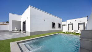 Un edificio moderno con piscina, un patio con sillones de descanso y un cielo azul despejado.