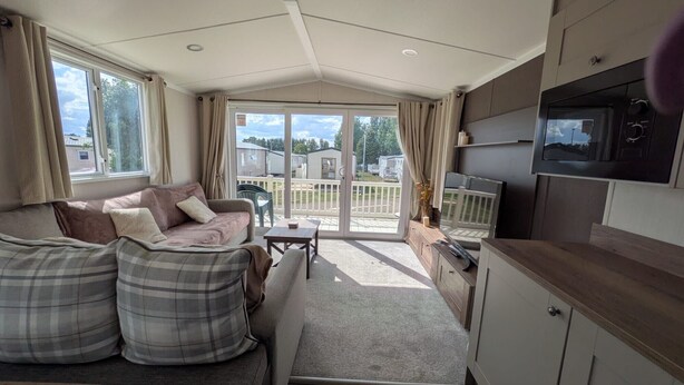 A caravan-style living area with a sofa, a small table, and a TV mounted on the wall. - Seaside Hunstanton Manor Park 2026 Model (Hunstanton)