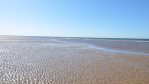 Ein Strand mit weitem Sandstreifen und sanften Wellen.