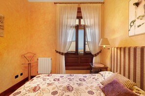 A hotel room with a bed, a window with curtains, a bedside table, a lamp, and a radiator. - Vacation Apartment 'Finca Robles 2' with Sea View, Wi-Fi and Air Conditioning (La Orotava)