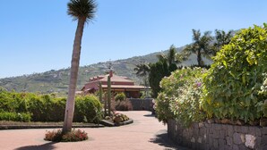A pathway leading to a building with a red roof, surrounded by greenery and a clear sky.