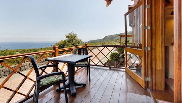 A wooden deck with a table and chairs, a glass door, and a view of the ocean.