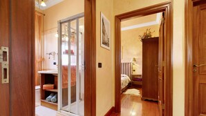 A hallway with wooden doors, a glass door leading to a bathroom, and a bed in the background.