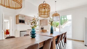 Uma cozinha moderna com armários de madeira, uma área de jantar com uma mesa comprida e luminárias pendentes de vime.