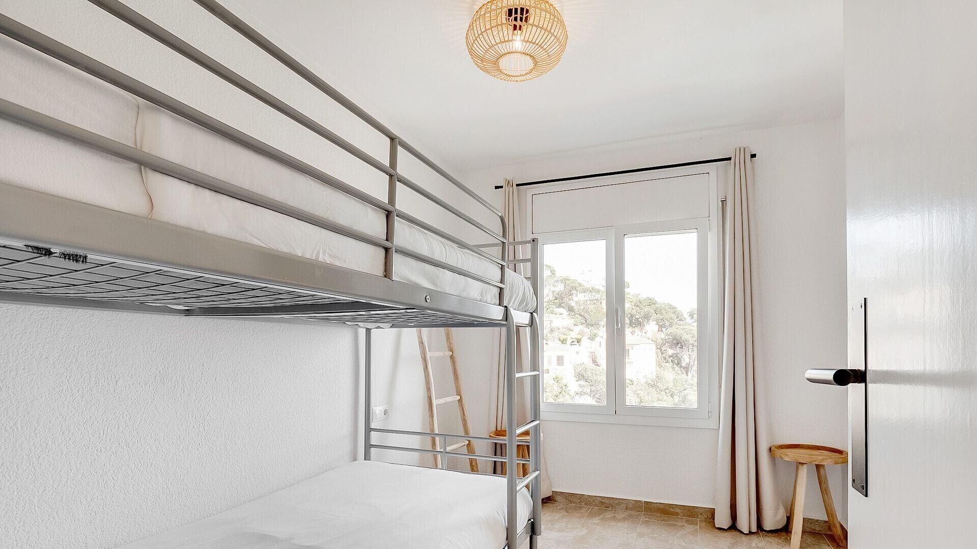 Een kamer met een stapelbed, een ladder, een raam met gordijnen en een deur.