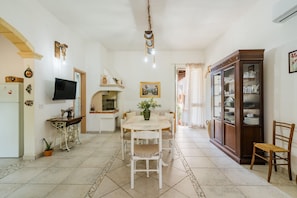 A kitchen with a dining table, chairs, a TV, a sewing machine, and a cabinet.