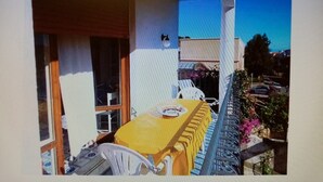 Un balcon avec une table et des chaises, une fenêtre et une vue sur la rue.