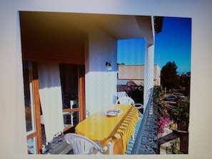 Un balcon avec une table et des chaises, une fenêtre et une vue sur la rue.