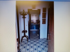 Un corridoio con pavimento piastrellato, una porta in legno e una cucina visibile sullo sfondo.