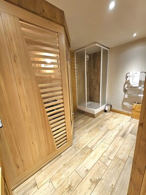 A room with a wooden floor, a sliding door, a shower area, and a small wooden cabinet. - Apartment 'Hameau du Soleil Val Thorens 17' with Mountain View and Balcony (Les Belleville)