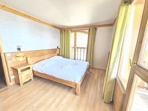 Ein Schlafzimmer mit einem hölzernen Bett, Nachttischen, einem Fenster mit Vorhängen und Blick ins Freie.